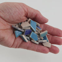 Video of Flip ceramic puzzle pieces in blue mix, opaque glazed porcelain, 4–20 mm, held in a hand and poured out to show their shapes and finish