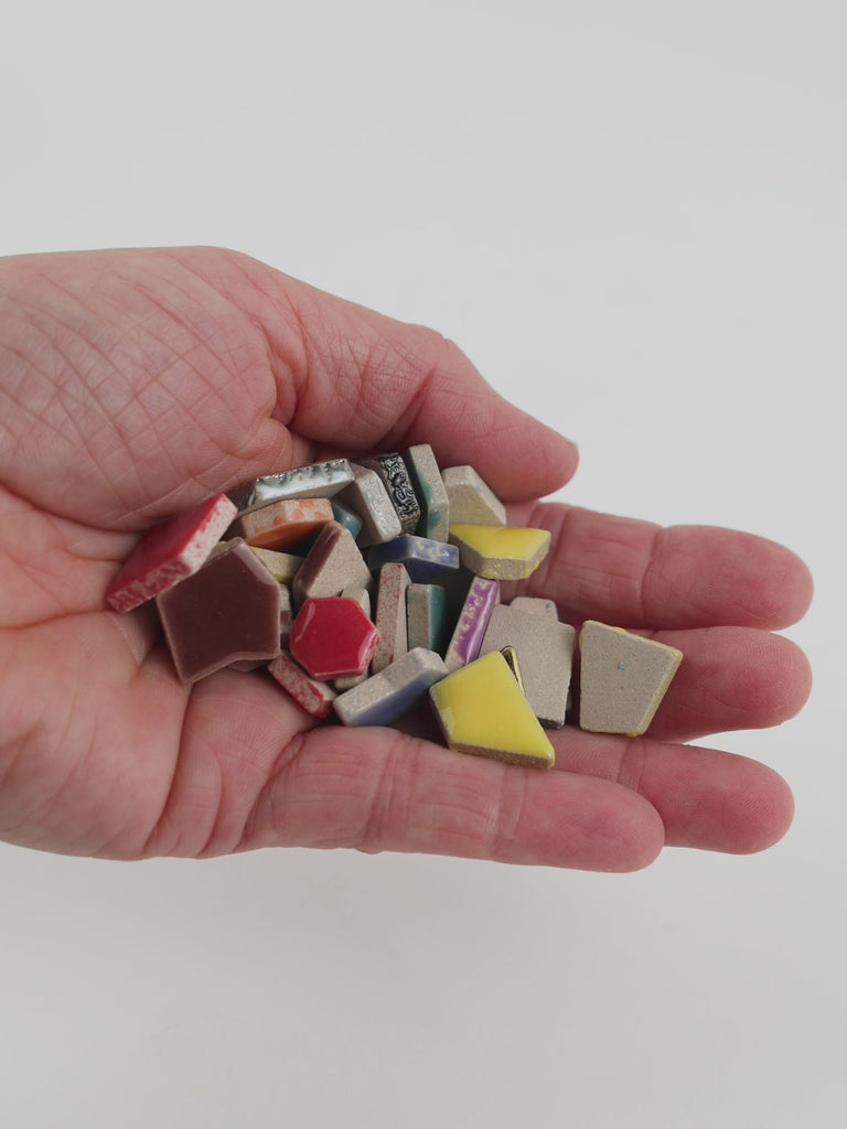 Video of Flip ceramic puzzle pieces in tropical mix, opaque glazed porcelain, 4–20 mm, held in a hand and poured out to show their shapes and finish