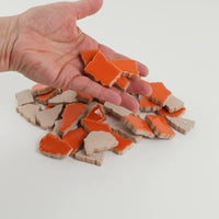 Video of Flip XL ceramic puzzle pieces in mandarin, opaque glazed porcelain, 20–60 mm, picked up from a pile by hand and dropped back to show their size, shapes and finish