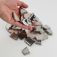 Video of Flip XL ceramic puzzle pieces in silver, opaque glazed porcelain, 20–60 mm, picked up from a pile by hand and dropped back to show their size, shapes and finish