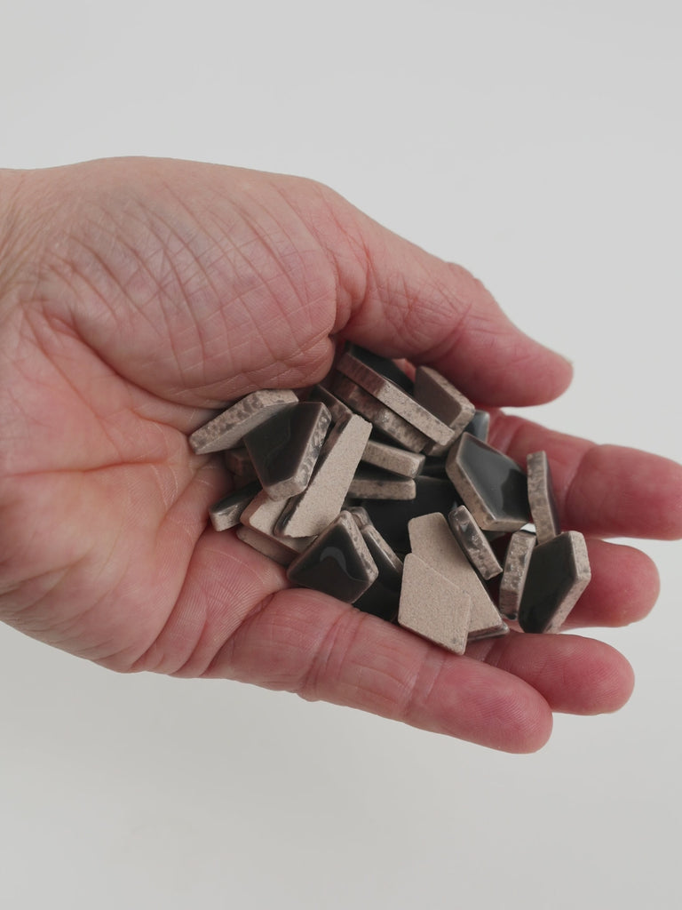 Video of Flip ceramic puzzle pieces in anthracite, opaque glazed porcelain, 4–20 mm, held in a hand and poured out to show their shapes and finish