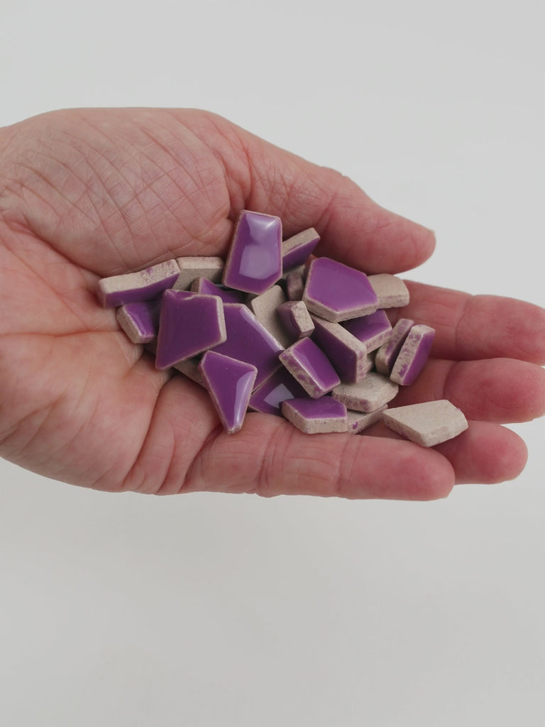 Video of Flip ceramic puzzle pieces in purple, opaque glazed porcelain, 4–20 mm, held in a hand and poured out to show their shapes and finish