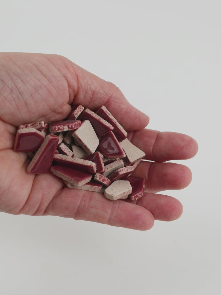 Video of Flip ceramic puzzle pieces in old pink, opaque glazed porcelain, 4–20 mm, held in a hand and poured out to show their shapes and finish