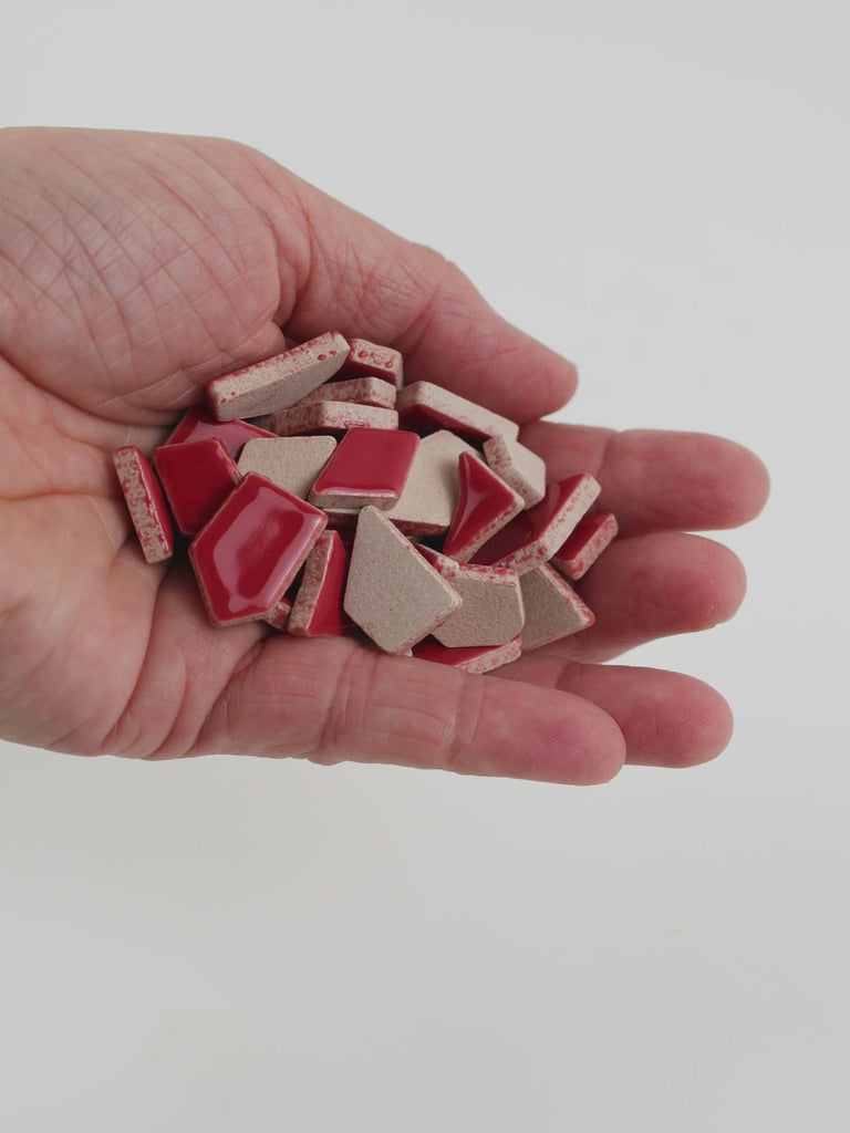 Video of Flip ceramic puzzle pieces in cherry red, opaque glazed porcelain, 4–20 mm, held in a hand and poured out to show their shapes and finish